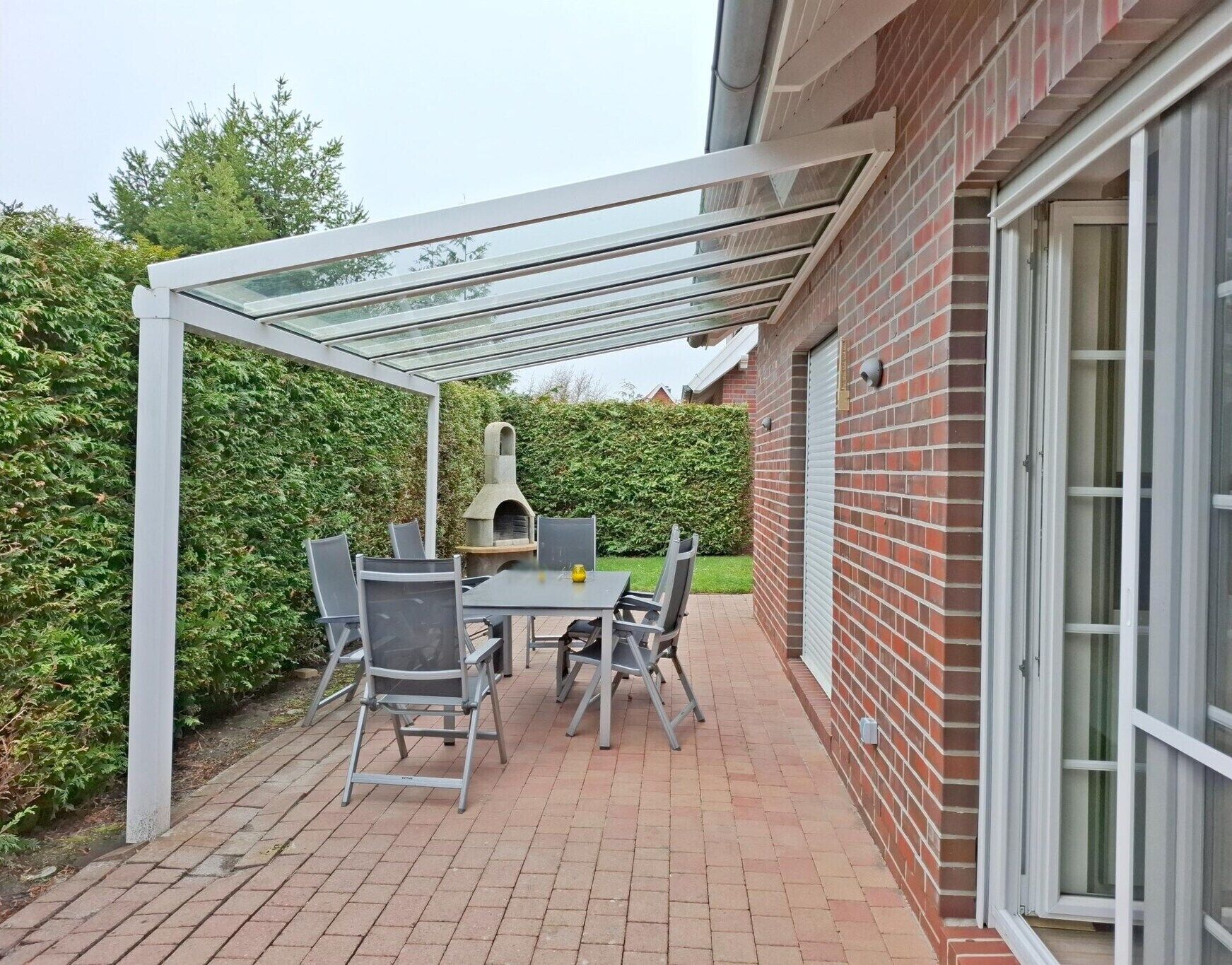 A covered patio with a brick wall, a brick chimney, and a table with chairs.