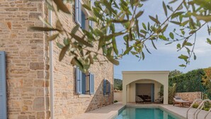 Ein Steinhäuschen mit Pool, Sitzgelegenheiten im Freien und einer überdachten Terrasse mit Tisch und Stühlen.