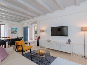 Ein modernes Wohnzimmer mit einer Couch, einem Couchtisch, einem Fernseher und einem Essbereich mit Stühlen und Tisch.