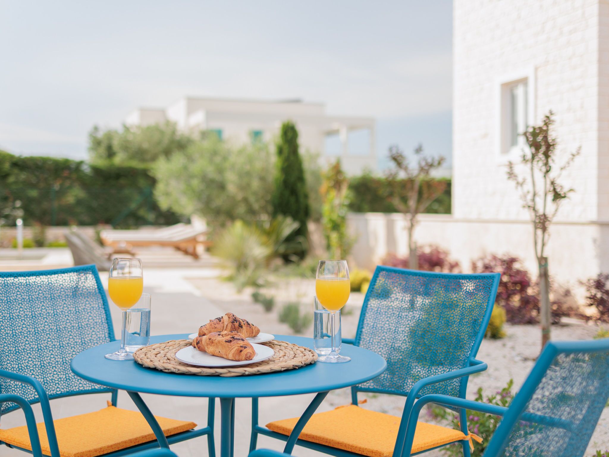 An outdoor seating area with a table and chairs, a croissant, and glasses of orange juice.