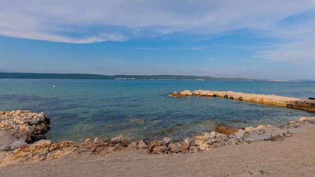 Eine Küstenlandschaft mit klarem Wasser, felsigem Ufer und weit entfernten Hügeln.
