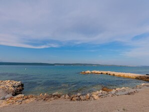 Eine Küstenlandschaft mit klarem Wasser, felsigem Ufer und weit entfernten Hügeln.