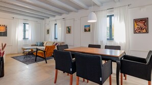 Ein modernes Wohnzimmer mit Essbereich, mit einem großen Holztisch, schwarzen Stühlen, einer Couch und einer Decke mit freiliegenden Balken.