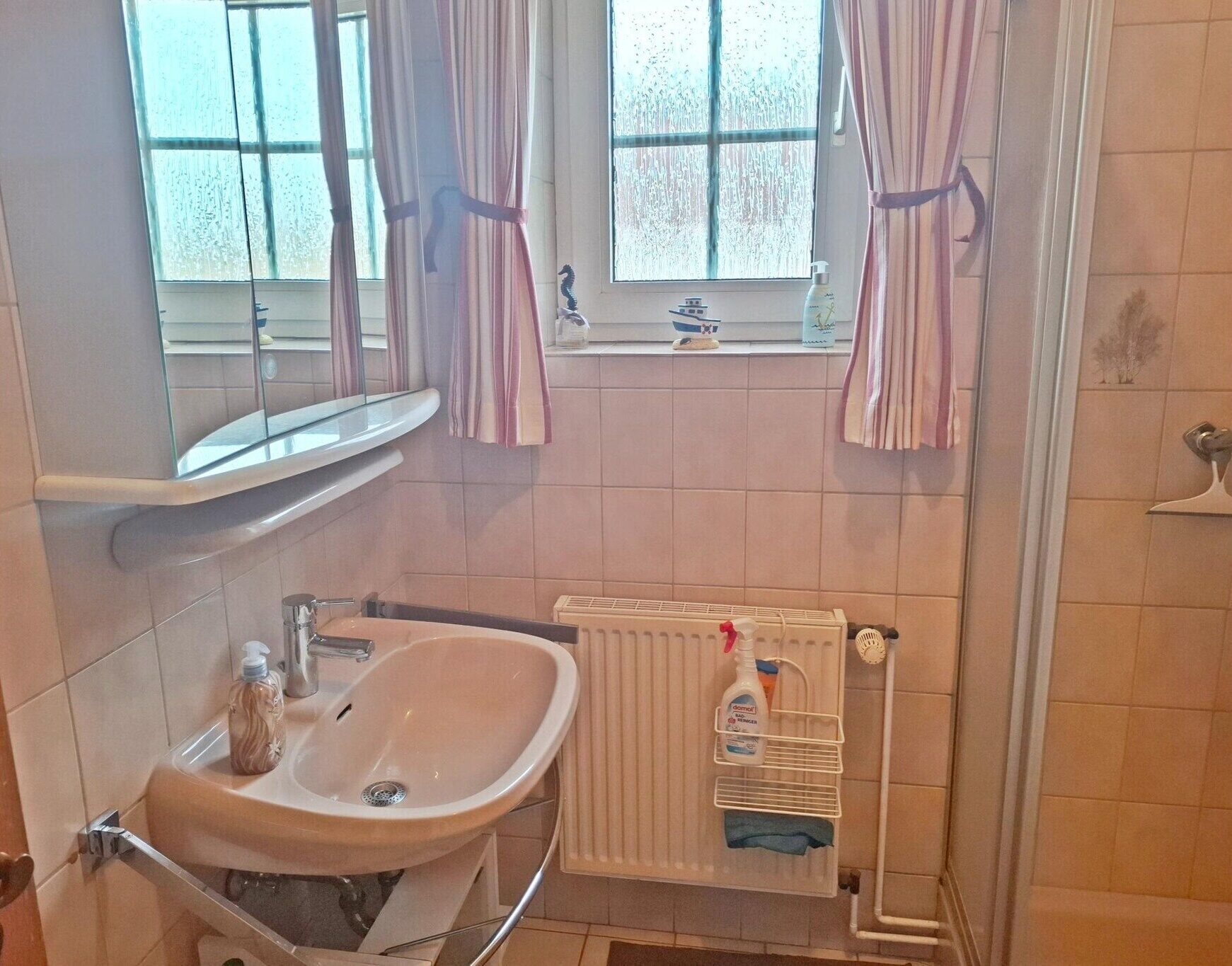 A bathroom with a sink, mirror, window with curtains, and a radiator.