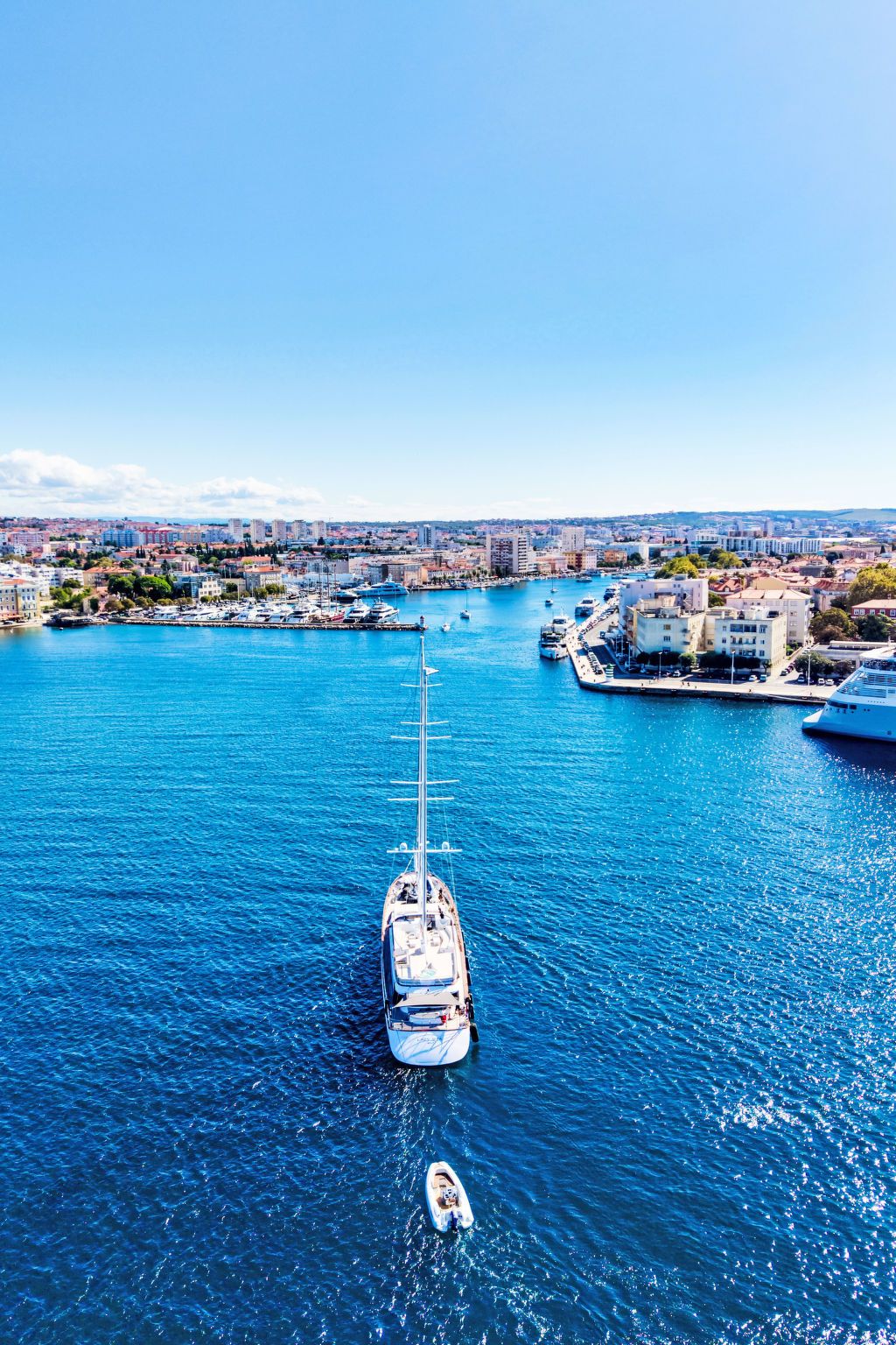 A marina with boats docked, a large cruise ship, and a cityscape in the background.