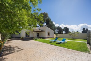 Ein Haus mit gepflasterter Terrasse, zwei blauen Liegestühlen und einem kleinen Rasen.
