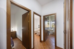 Ein Flur mit einem Bett, einem Nachttisch und einem Badezimmer mit Waschbecken und Spiegel.