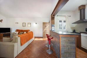 Ein Wohnzimmer mit Sofa, Fernseher und einer Küchenzeile mit Theke und Barhocker.