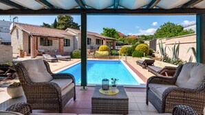 Ein überdachter Außenbereich mit Pool, Korbmöbeln und Blick auf benachbarte Häuser.