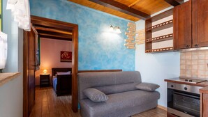 Ein gemütlicher Wohnbereich mit einer Couch, Holzboden, einer Küchenzeile mit Herd und einer blauen Wand mit einer Leuchte.