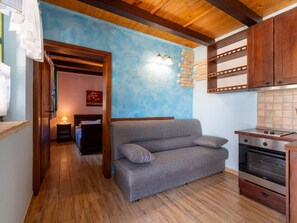 Ein gemütlicher Wohnbereich mit einer Couch, Holzboden, einer Küchenzeile mit Herd und einer blauen Wand mit einer Leuchte.