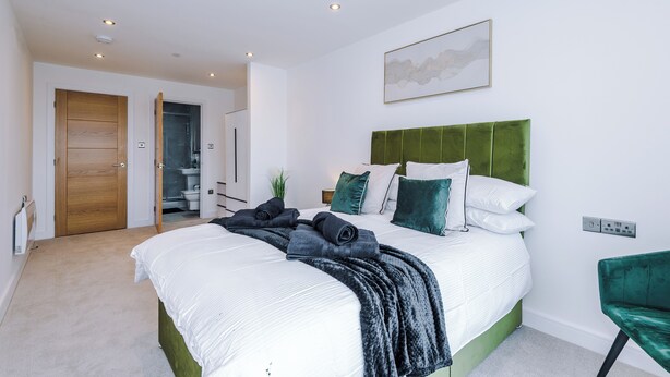 A bedroom with a bed, green upholstered headboard, white bedding, and a green chair. - Family Friendly Stay-Leeds City Centre With City View (Leeds)