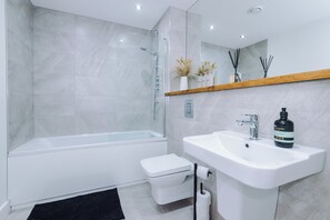 Un bany modern amb una dutxa amb envàs de vidre, un vàter blanc i un lavabo amb un mirall a sobre.