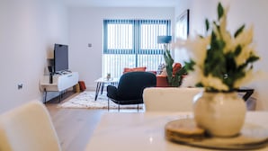 A modern living room with a sofa, a dining table, and a TV. - Family Friendly Stay-Leeds City Centre With City View (Leeds)