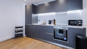 A modern kitchen with grey cabinets, a black oven, a microwave, and a coffee maker. - Family Friendly Stay-Leeds City Centre With City View (Leeds)