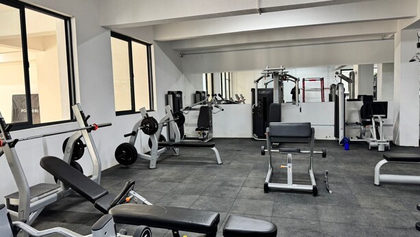 Uma academia com diversos equipamentos de exercício, incluindo esteiras, aparelhos de musculação e pesos livres.