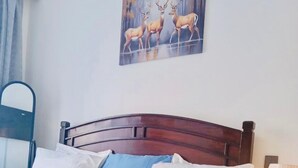 Uma cama com cabeceira de madeira, travesseiros brancos e azuis, uma mesa de cabeceira com abajur e um quadro de veados na parede.