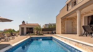 Ein Schwimmbecken mit einer gefliesten Kante, umgeben von Liegestühlen und einer Terrassenanlage.
