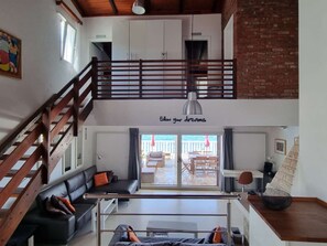 A spacious living area with a high ceiling, a staircase, a balcony with outdoor furniture, and a motivational quote on the wall. - Vacation home  by Interhome (Blato)