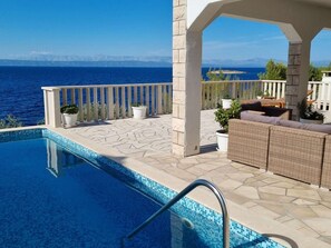 A swimming pool with a view of the sea and mountains, outdoor seating, and a white railing. - Vacation home  by Interhome (Blato)