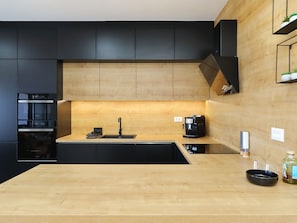 A modern kitchen with black cabinetry, a wooden countertop, a built-in oven, a coffee machine, and a sink. - Vacation home  by Interhome (Vrsi)