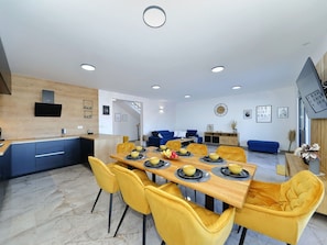 A modern kitchen with a built-in oven and a dining area with a wooden table and yellow chairs. - Vacation home  by Interhome (Vrsi)