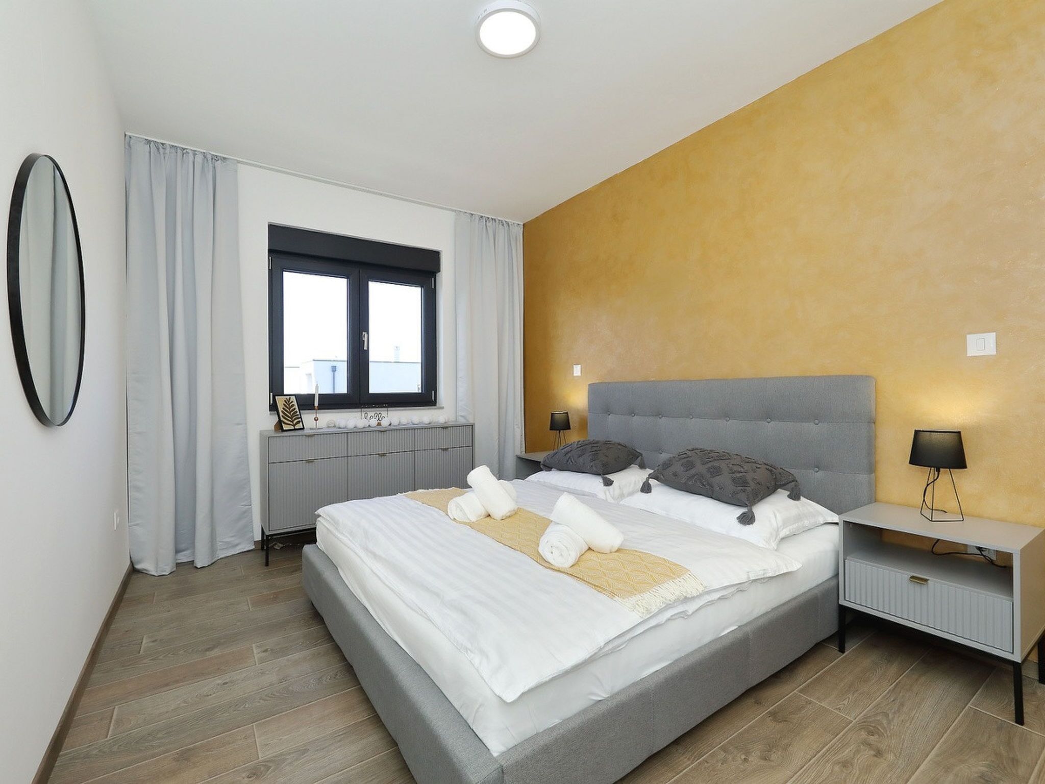 Une chambre à coucher moderne avec un grand lit, une table de chevet, un miroir et une fenêtre avec des rideaux.