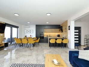 A modern kitchen with a central island, dining area with yellow chairs, and a living room with a blue sofa. - Villa Good Vibes with heated pool by Interhome (Vrsi)