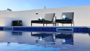 En pool med två solstolar och ett litet svart skåp.