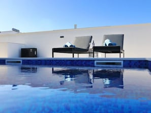 A swimming pool with two lounge chairs and a small black cabinet. - Vacation home  by Interhome (Vrsi)