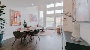 A modern living room with a dining area, large windows, and artwork on the walls.