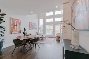 A modern living room with a dining area, large windows, and artwork on the walls. - 3BR | Garage | DT Views | Central | Lux Townhome (Calgary)