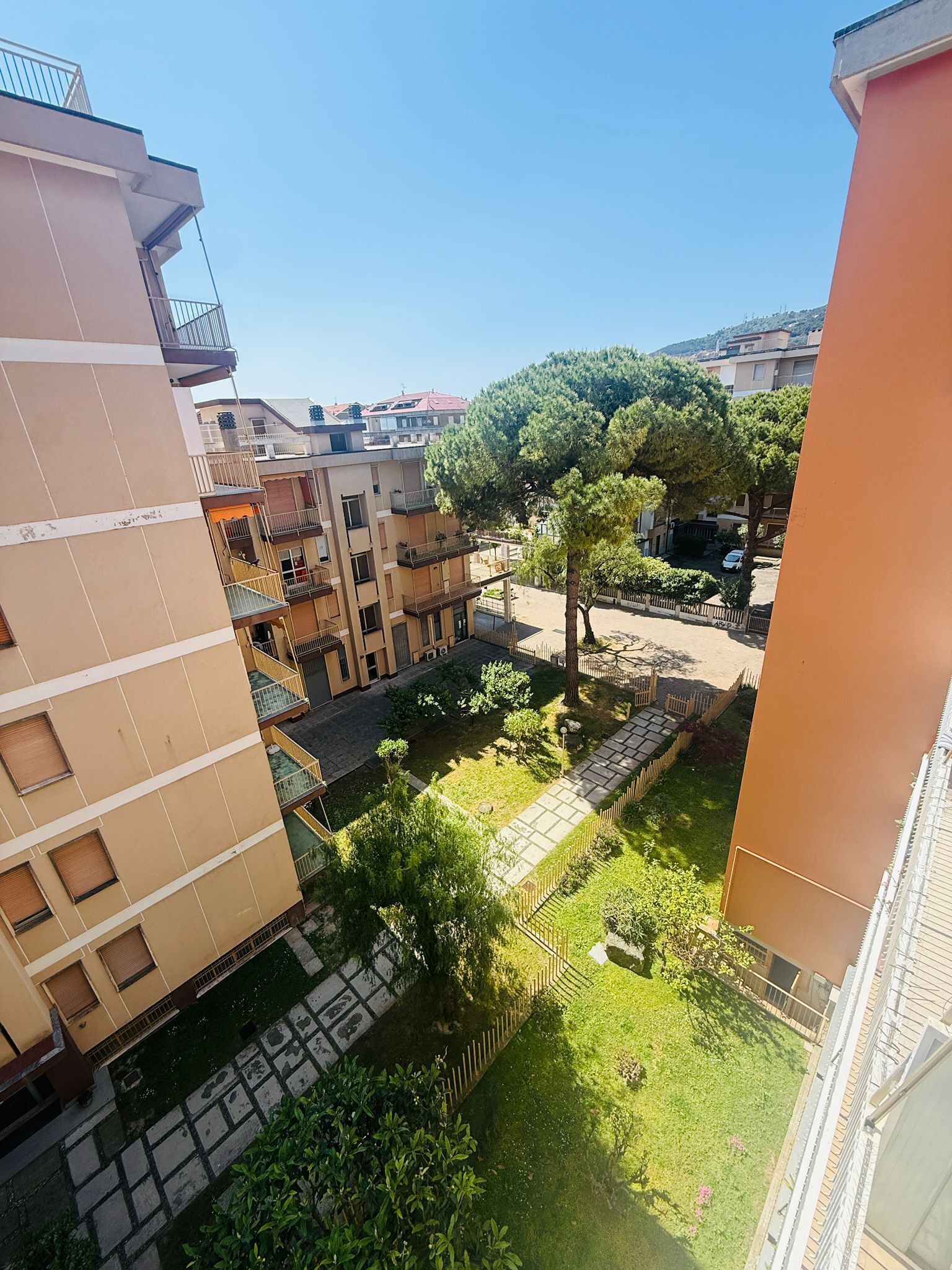 A residential area with multi-story buildings, a central courtyard with trees, and a clear sky.