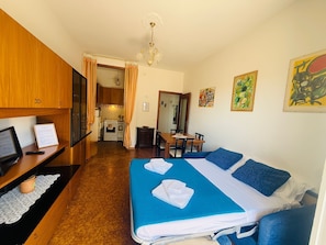 Ein Hotelzimmer mit Bett, Schreibtisch mit Computer, einer Küchenzeile und einem Essbereich.