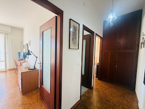 Ein Flur mit Holztür, Schreibtisch mit Computer, Lampe und großem Kleiderschrank.