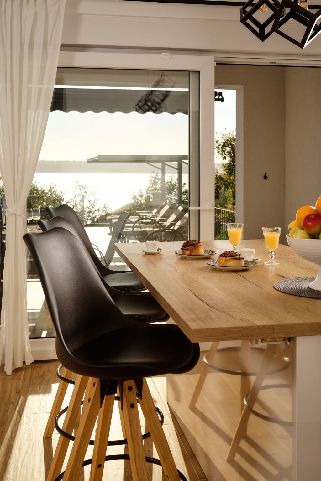 Un comedor con mesa de madera, sillas negras y vista al mar.