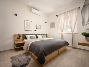 A modern bedroom with a wooden bed, a bedside table, a nightstand, a wall-mounted air conditioner, and a window with curtains. - Beautiful Villa Katharina with pool by Interhome (Rovanjska)