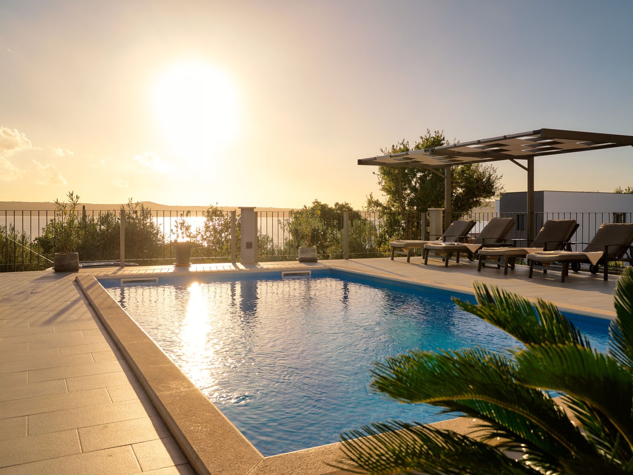 Una piscina con sillones de descanso y una pérgola, rodeada de plantas y vistas al mar.