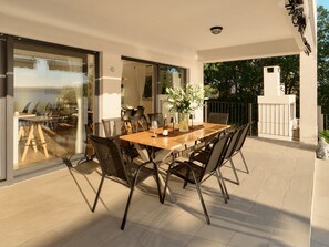 A dining area with a table and chairs, a vase with flowers, and a view through glass doors.
