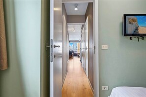 A hallway leading to a bedroom with a bed, a television mounted on the wall, and a door at the end. - Stylish renovated 2-bedroom apartment in with garage (Knokke-Heist)