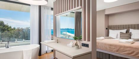 A modern bathroom with a freestanding bathtub, a large mirror, and a view of the sea.