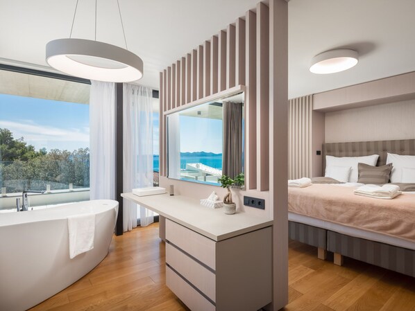 Un bagno moderno con una vasca da bagno indipendente, uno specchio grande e vista sul mare.