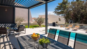 A modern outdoor pool area with a pergola, seating, and a view of the surrounding landscape. - Villa Acacia with heated pool by Interhome (Petrčane)