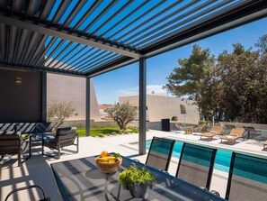 Ein moderner Poolbereich im Freien mit einer Pergola, Sitzgelegenheiten und Blick auf die umliegende Landschaft.