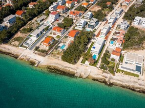 Eine Luftaufnahme einer Küstenwohngegend mit modernen Häusern, einem klaren Strand und ruhigem Meer.