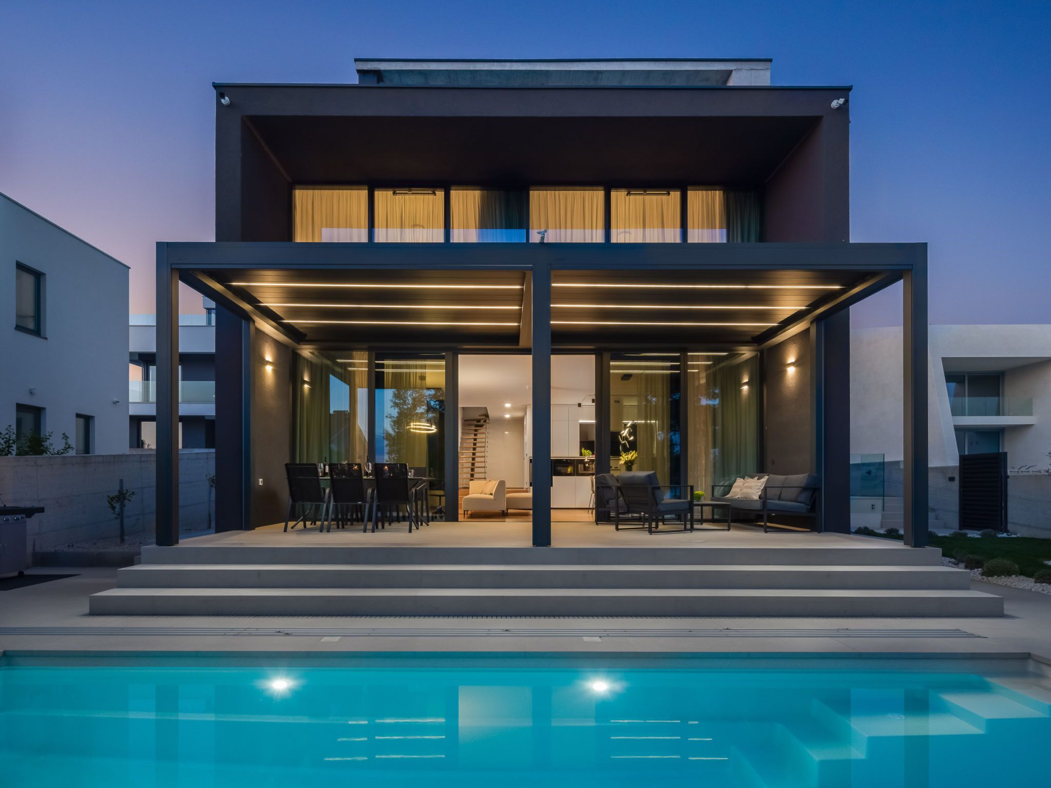 Une maison moderne à deux étages, dotée d’un espace extérieur aménagé et couvert, ainsi que d’une piscine.