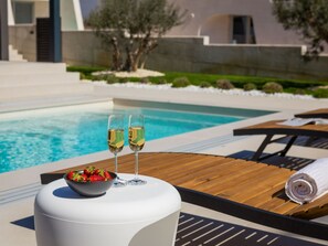 A poolside setting with two glasses of champagne, a bowl of strawberries, and a wooden lounge chair with a towel. - Villa Acacia with heated pool by Interhome (Petrčane)