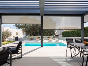 Un'area piscina moderna all'aperto, con lettini e un tavolo, circondata da una struttura in vetro.