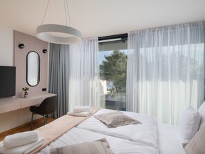 Ein modernes Schlafzimmer mit einem Bett, einem Schreibtisch, einem Stuhl, einem Fernseher und einem großen Fenster mit Vorhängen.