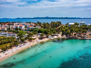 Una cittadina costiera con una spiaggia, acque turchesi cristalline e edifici dai tetti rossi.